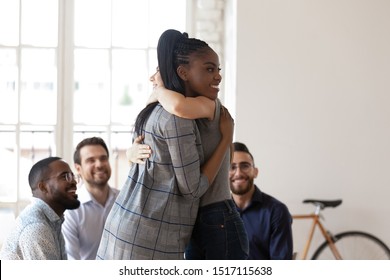 Happy african american manager hugging smiling female colleague at team building activity. Two friendly coworkers embracing at group therapy session. Joyful diverse team supporting each other.