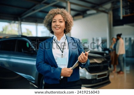 Happy African American mature saleswoman at car dealership looking at camera.