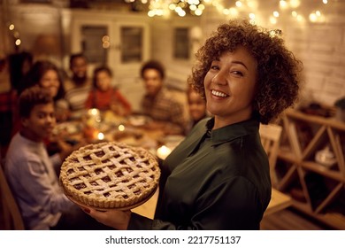 Happy African American mature woman carrying Thanksgiving pie while serving food to her family in dining room and looking at camera. - Powered by Shutterstock