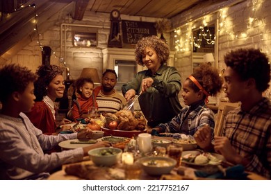 Happy African American mature woman carving turkey meat while having Thanksgiving dinner with her family. - Powered by Shutterstock