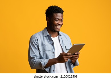 Happy African American Millennial Guy Using Modern Digital Tablet, Looking At Gadget Screen And Smiling On Yellow Studio Background, Black Man Gambling Or Shopping Online, Copy Space