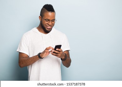 Happy african American millennial male gadget use isolated on blue studio background typing on smartphone, smiling biracial man browsing wireless internet on modern cellphone, blank copy space