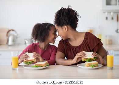 Happy African American Mom And Daughter Enjoying Time Together At Home, Having Lunch, Drinking Fresh Orange Juice, Eating Sandwiches, Touching Each Other With Foreheads And Smiling, Copy Space