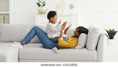 Happy african american mom playing funny game with little cute girl at home. 