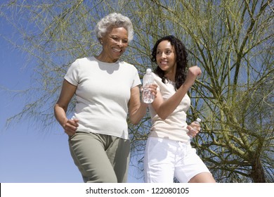 Happy African American Mother And Daughter Jogging Together Against Blue Sky
