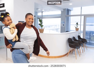 Happy african american mother and daughter walking in waiting room at hospital, copy space. Hospital, motherhood, family, medicine and healthcare, unaltered. - Powered by Shutterstock