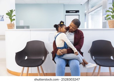 Happy african american mother and daughter sitting in waiting room at hospital, copy space. Hospital, motherhood, family, medicine and healthcare, unaltered. - Powered by Shutterstock