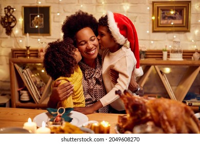 Happy African American mother enjoying while her children are kissing her at dining table for Christmas. - Powered by Shutterstock