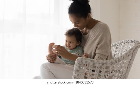 Happy African American mother have fun play with little newborn baby child at home. Smiling biracial young mom sit in chair at home enjoy playful time with cute small ethnic toddler kid daughter.