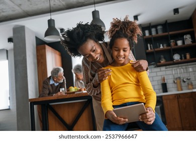 Happy african american mother helps teenage daughter with homework using digital tablet - Powered by Shutterstock