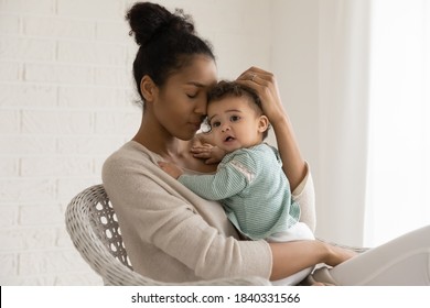 Happy African American Mother Hold Hug Newborn Small Biracial Daughter Shown Love And Care. Smiling Ethnic Mom Embrace Cuddle Toddler Baby Child Relax In Chair At Home Together. Childcare Concept.