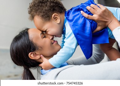 Happy African American Mother Holding Little Son In Superhero Costume At Home