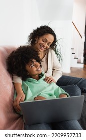 Happy African American Mother Hugging Cheerful Preteen Daughter Near Laptop