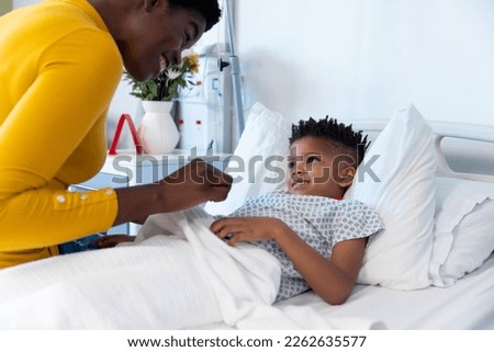 Happy african american mother sitting with son patient in hospital bed, smiling with copy space. Hospital, medical and healthcare services.
