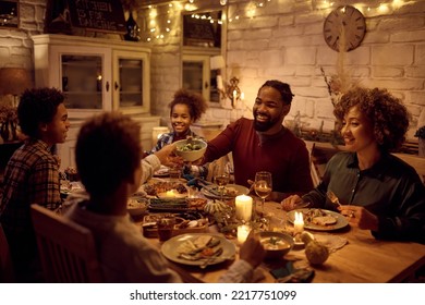 Happy African American Multigeneration Family Eating At Dining Table While Celebrating Thanksgiving. Focus Is On Father Passing Food To His Son.