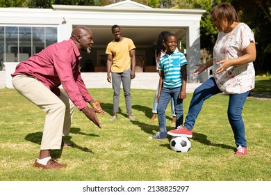 Happy african american multi-generational family playing soccer together in front yard on sunny day. unaltered, family, togetherness, weekend and leisure concept.