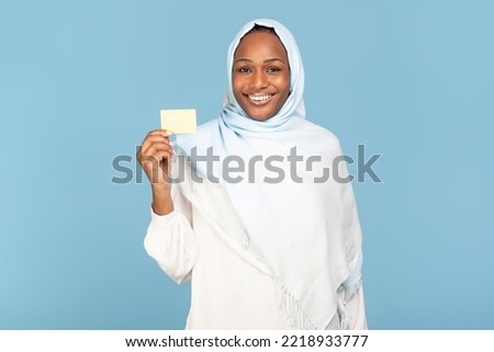 Happy african american muslim woman in hijab holding golden credit card advertising bank service over blue background and smiling to camera. Easy banking, money and payment concept