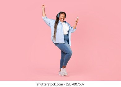 Happy African American Obese Woman Listening To Music On Phone Wearing Headphones Dancing And Singing Having Fun Over Pink Studio Background. Great Playlist Concept. Full Length - Powered by Shutterstock