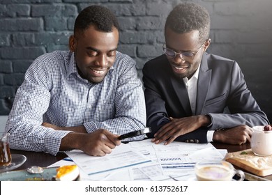 Happy African American Office Workers Dressed In Formal Clothing Having Cheerful Looks, Studying And Amalyzing Legal Documents On Table Using Magnifying Glass While Getting Papers Ready For Meeting