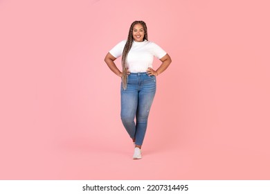 Happy African American Oversized Black Woman Standing Holding Hands On Hips Wearing Plus Size Clothes Posing Smiling To Camera Over Pink Studio Background. Full Length