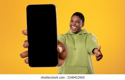 Happy african american oversized woman demonstrating cellphone with blank screen and showing thumb up, plump lady holding smartphone with copy space for ad, mockup
