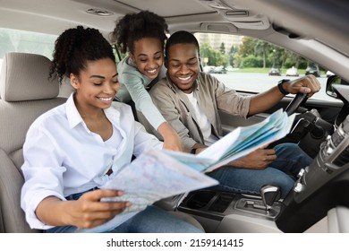 Happy African American Parents And Daughter Sitting In Car Holding Map For Navigation, Planning Summer Road Trip. Family Enjoying Auto Tourism Traveling Together On Vacation