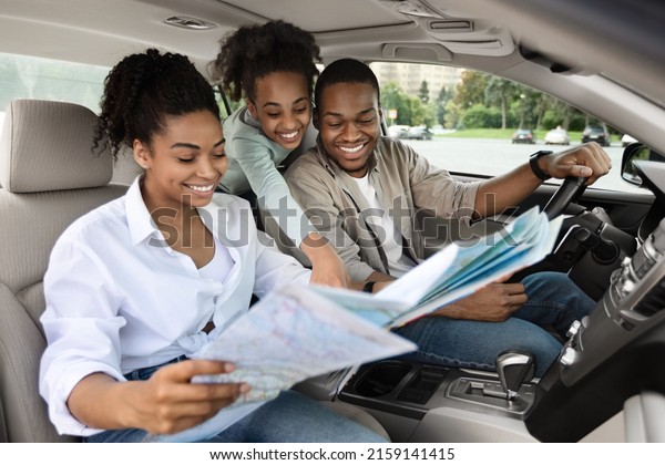 Happy African\
American Parents And Daughter Sitting In Car Holding Map For\
Navigation, Planning Summer Road Trip. Family Enjoying Auto Tourism\
Traveling Together On\
Vacation