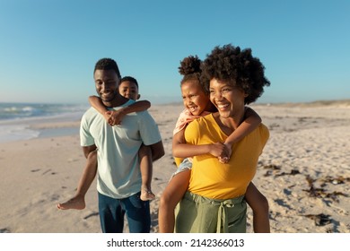 Happy african american parents giving piggyback to children while walking at beach on sunny day. unaltered, family, lifestyle, togetherness, enjoyment and holiday concept. - Powered by Shutterstock