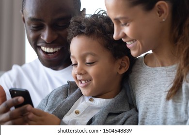 Happy African American Parents With Little Son Using Phone Close Up, Looking At Screen, Family Playing Mobile Game, Browsing Apps, Mother, Smiling Father And Child Watching Funny Video Online