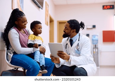 Happy African American pediatrician using digital tablet while communicating with a boy and his mother in hallway at medical clinic.  - Powered by Shutterstock