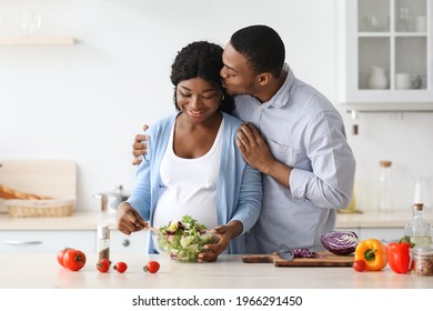 Happy african american pregnant couple cooking healthy meal together. Positive expecting black woman and man making dinner at home, making salad from fresh vegetables, kitchen interior - Powered by Shutterstock