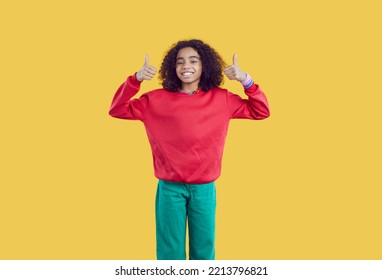 Happy African American Pretten Girl On Yellow Background Showing Thumbs Up Recommending Best Choice. Portrait Of Positive Cute Curly Ethnic Teen Girl Dressed In Casual Clothes Showing Two Thumbs Up.