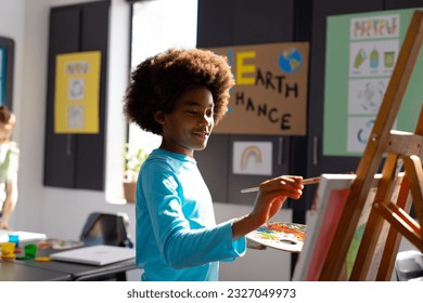 Happy african american schoolboy painting using brush and easel in school art class. School, education, creativity and learning concept. - Powered by Shutterstock