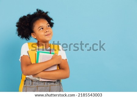 Happy African American schoolgirl holding books on blue background, back to school concept.