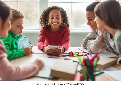 Happy African American Schoolgirl Using Phone Sitting With Classmates At Desk In Modern Classroom Indoors. School Education, Technology And Gadgets. Selective Focus - Powered by Shutterstock