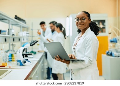 Happy African American scientist using laptop while working in lab and looking at camera. - Powered by Shutterstock