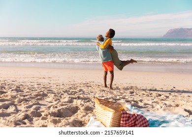 Happy african american senior man carrying mature woman while standing at beach against sea and sky. - Powered by Shutterstock