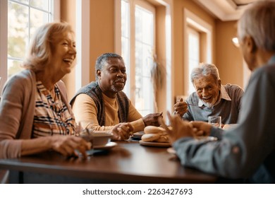 Happy African American senior man talking to his friends while eating at dining table at nursing home. - Shutterstock ID 2263427693