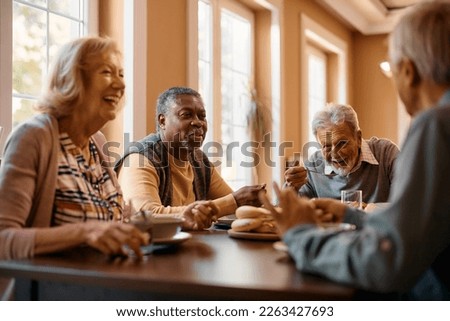Happy African American senior man talking to his friends while eating at dining table at nursing home.