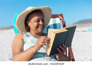 Happy african american senior woman reading book while sitting on folding chair at beach. unaltered, hobbies, active lifestyle, enjoyment and holiday concept. - Powered by Shutterstock