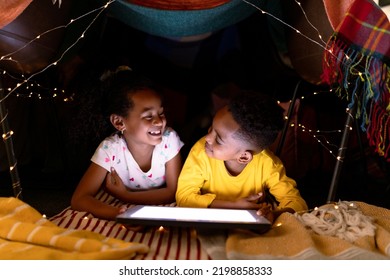 Happy african american siblings lying in makeshift tent, using tablet. childhood, christmas, festivity and tradition at home. - Powered by Shutterstock