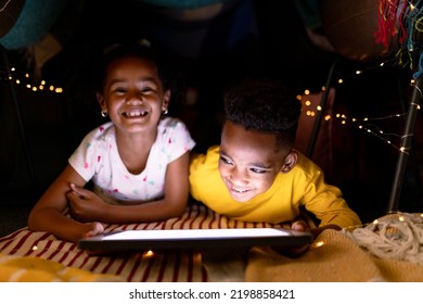 Happy african american siblings lying in makeshift tent, using tablet. childhood, christmas, festivity and tradition at home. - Powered by Shutterstock