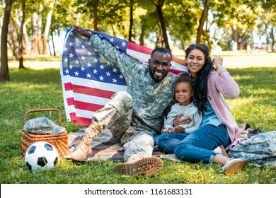 happy african american soldier in military uniform and family holding american flag in park