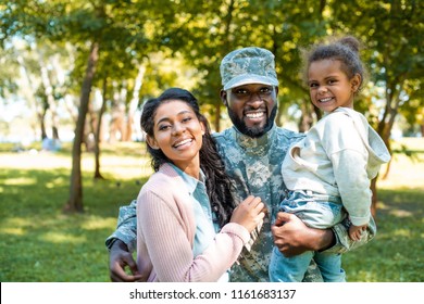 Happy African American Soldier In Military Uniform Looking At Camera With Family In Park