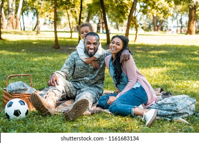 Happy African American Soldier Sitting On Grass With Family In Park