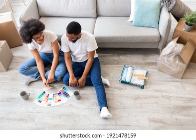 Happy African American Spouses Choosing Color Palette For Wall Painting During Renovation Sitting On Floor At Home. Interior Design Trends Concept. High-Angle View