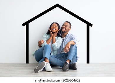 Happy african american spouses sitting near white wall and drawn house  dreaming   imagining their new home  planning relocation  creative collage