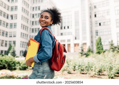 Happy African American Student Girl Posing With Backpack Holding Books Smiling Looking Aside Standing Near University Building Outdoor. Modern Education And Studentship Lifestyle