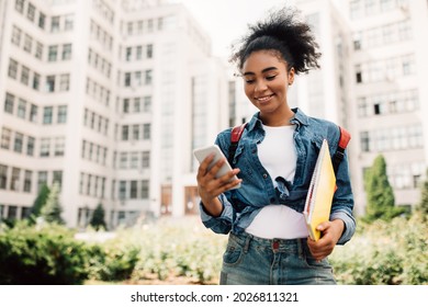 Happy African American Student Girl Using Phone With Educational App Standing Outdoors. Millennial Female Texting And Browsing Internet Via Smartphone Posing Near College Building - Shutterstock ID 2026811321
