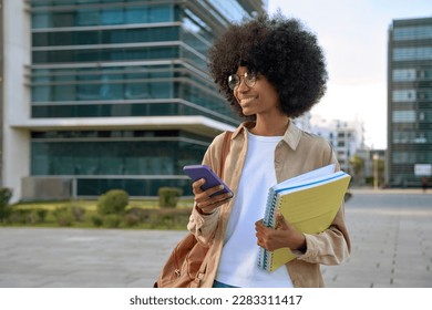 Happy African American student girl with afro haircut enjoy online communication, hold exercise books and backpack, scroll social media app on cell phone device, looking at camera on city street. - Powered by Shutterstock